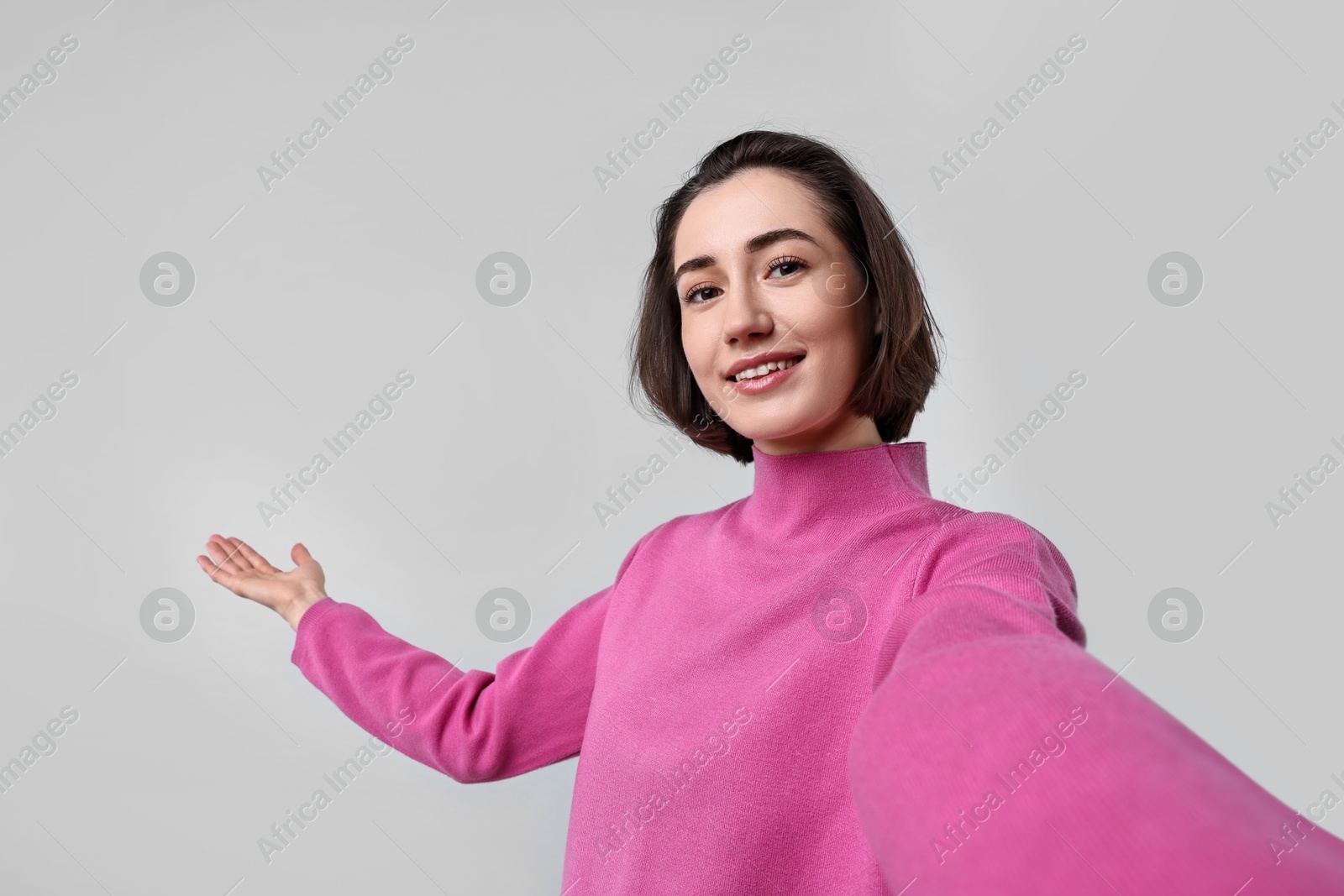 Photo of Cheerful woman welcoming friends or guests via video call on light grey background