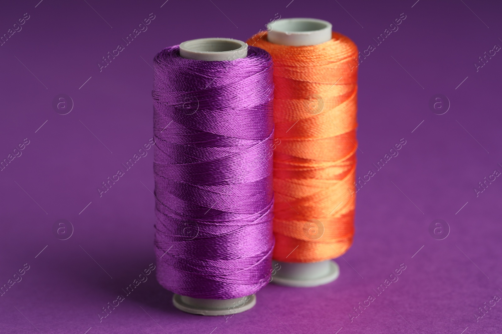 Photo of Different spools of sewing threads on violet background, closeup