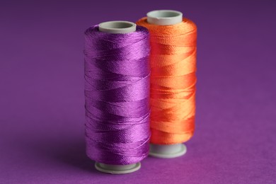 Photo of Different spools of sewing threads on violet background, closeup