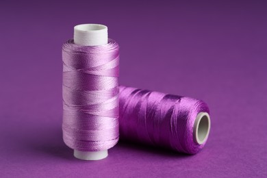 Photo of Spools of sewing threads on violet background, closeup