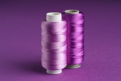 Photo of Spools of sewing threads on violet background, closeup