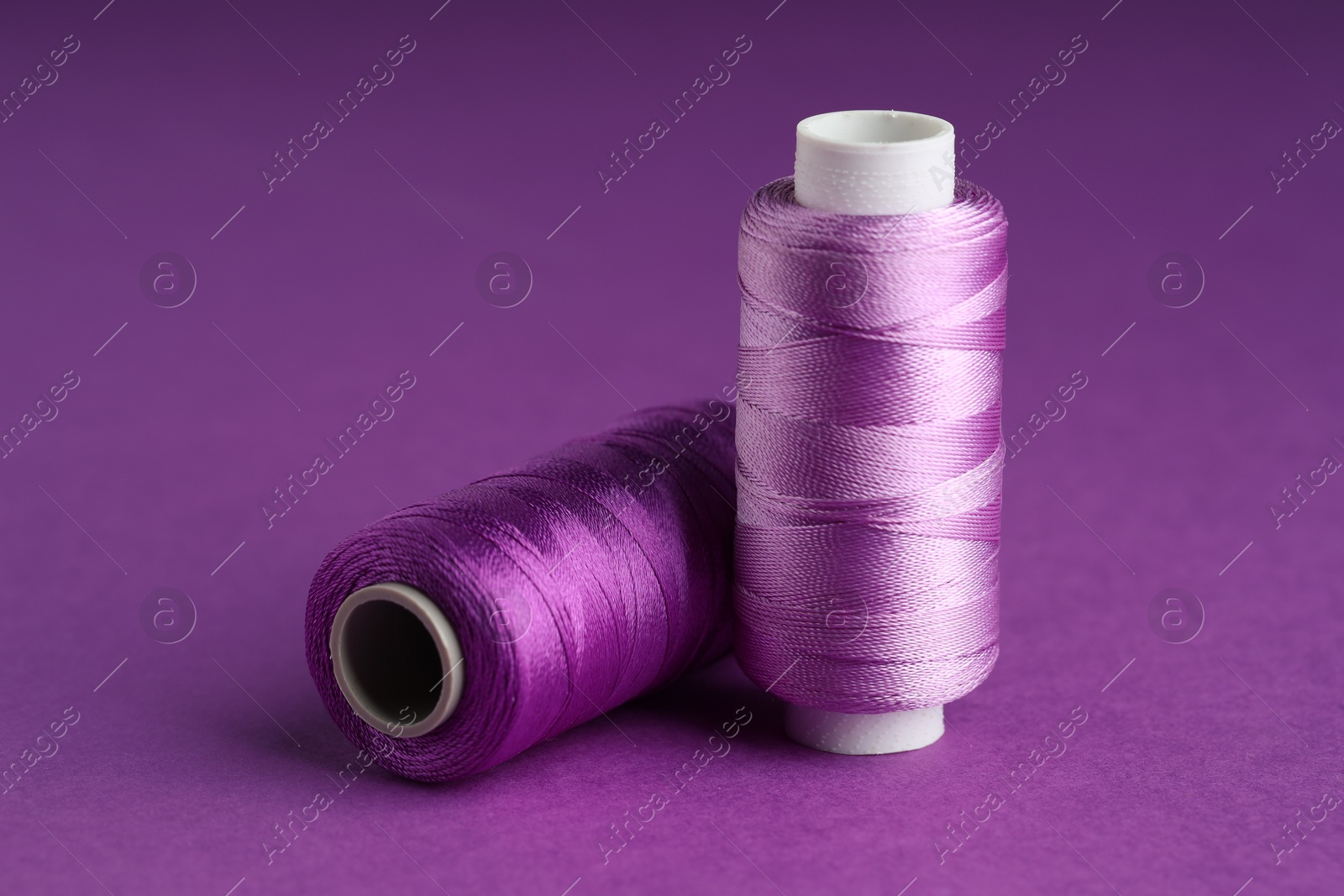 Photo of Spools of sewing threads on violet background, closeup