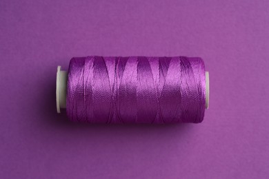 Photo of Spool of sewing thread on violet background, top view