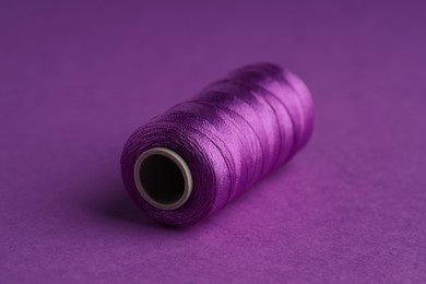 Photo of Spool of sewing thread on violet background, closeup