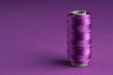 Photo of Spool of sewing thread on violet background, space for text