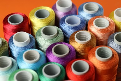 Photo of Different spools of sewing threads on orange background, closeup