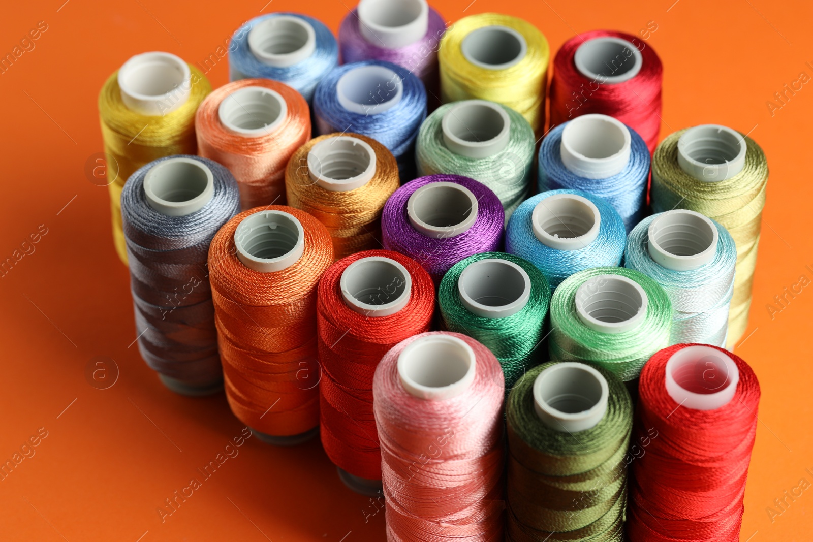 Photo of Different spools of sewing threads on orange background, closeup