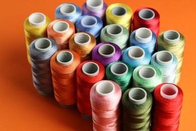 Photo of Different spools of sewing threads on orange background, closeup