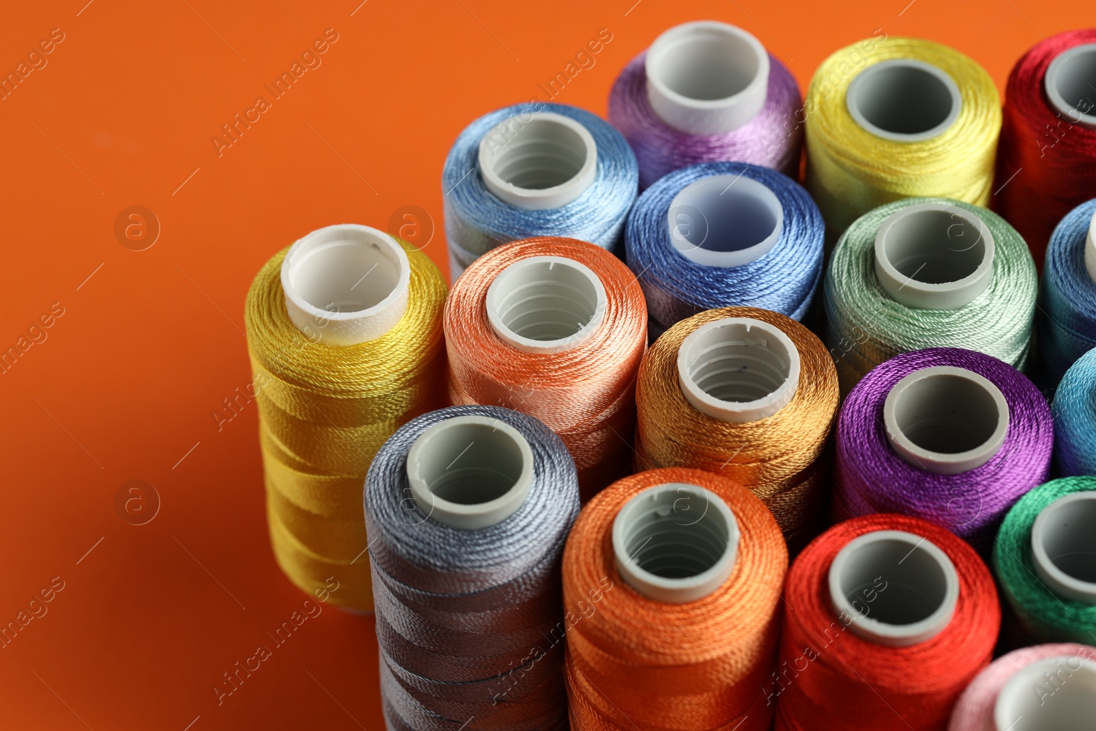 Photo of Different spools of sewing threads on orange background, closeup