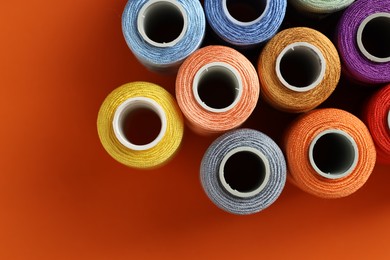 Photo of Different spools of sewing threads on orange background, flat lay. Space for text