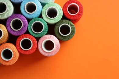 Photo of Different spools of sewing threads on orange background, flat lay. Space for text