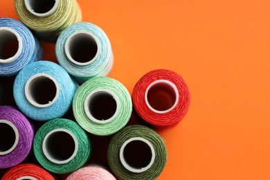 Photo of Different spools of sewing threads on orange background, flat lay. Space for text