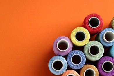 Photo of Different spools of sewing threads on orange background, flat lay. Space for text