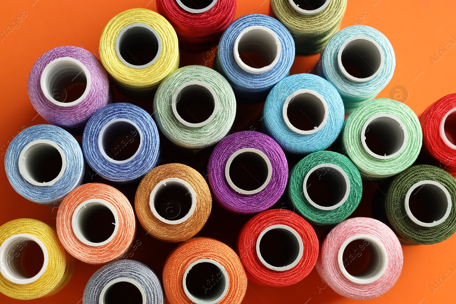 Photo of Different spools of sewing threads on orange background, flat lay