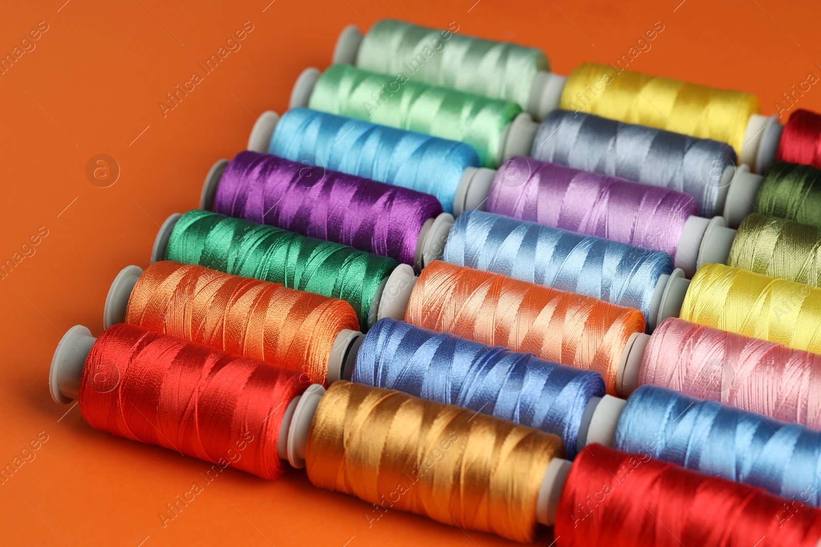 Photo of Different spools of sewing threads on orange background, closeup