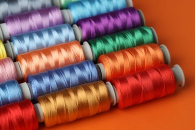 Photo of Different spools of sewing threads on orange background, closeup