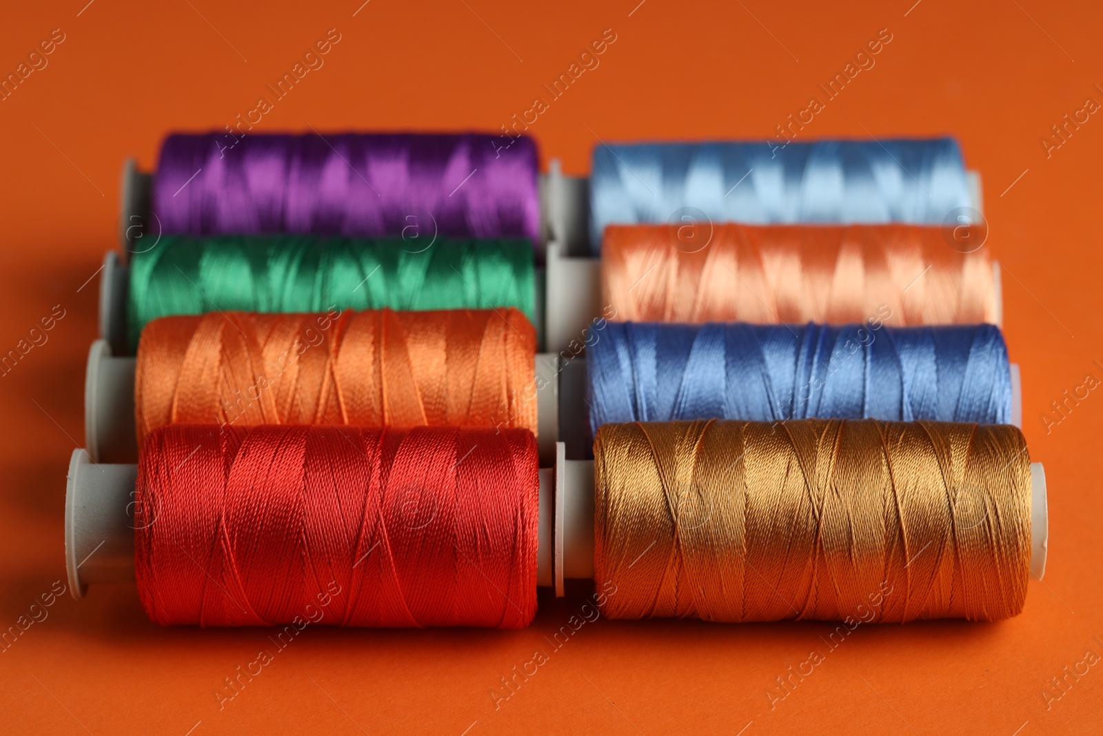 Photo of Different spools of sewing threads on orange background, closeup