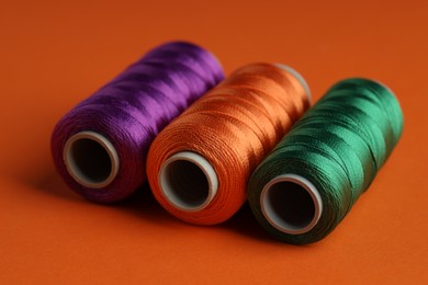 Photo of Different spools of sewing threads on orange background, closeup