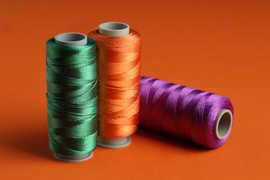 Photo of Different spools of sewing threads on orange background, closeup