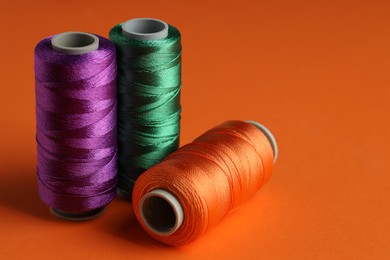 Different spools of sewing threads on orange background, closeup. Space for text