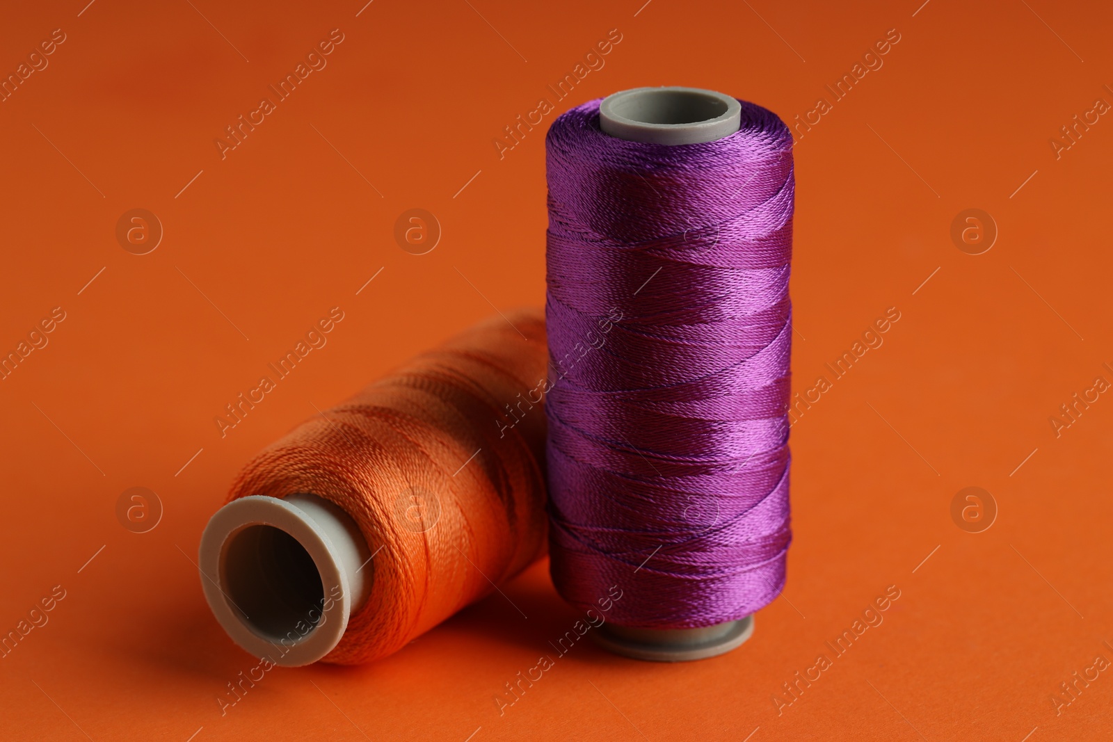 Photo of Different spools of sewing threads on orange background, closeup