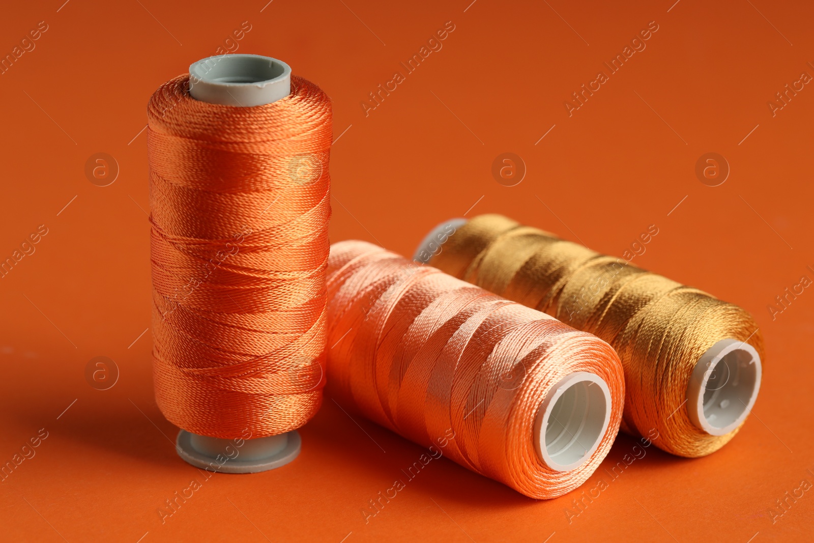 Photo of Different spools of sewing threads on orange background, closeup