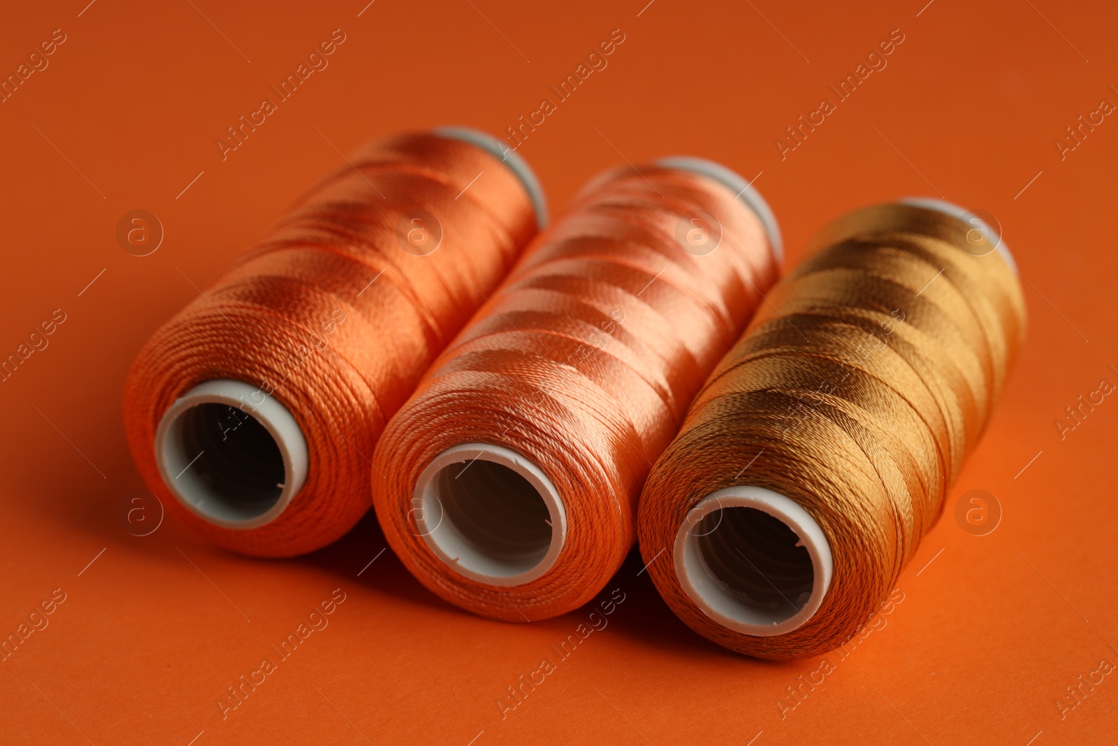 Photo of Different spools of sewing threads on orange background, closeup