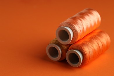 Different spools of sewing threads on orange background, closeup. Space for text