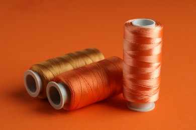 Photo of Different spools of sewing threads on orange background, closeup