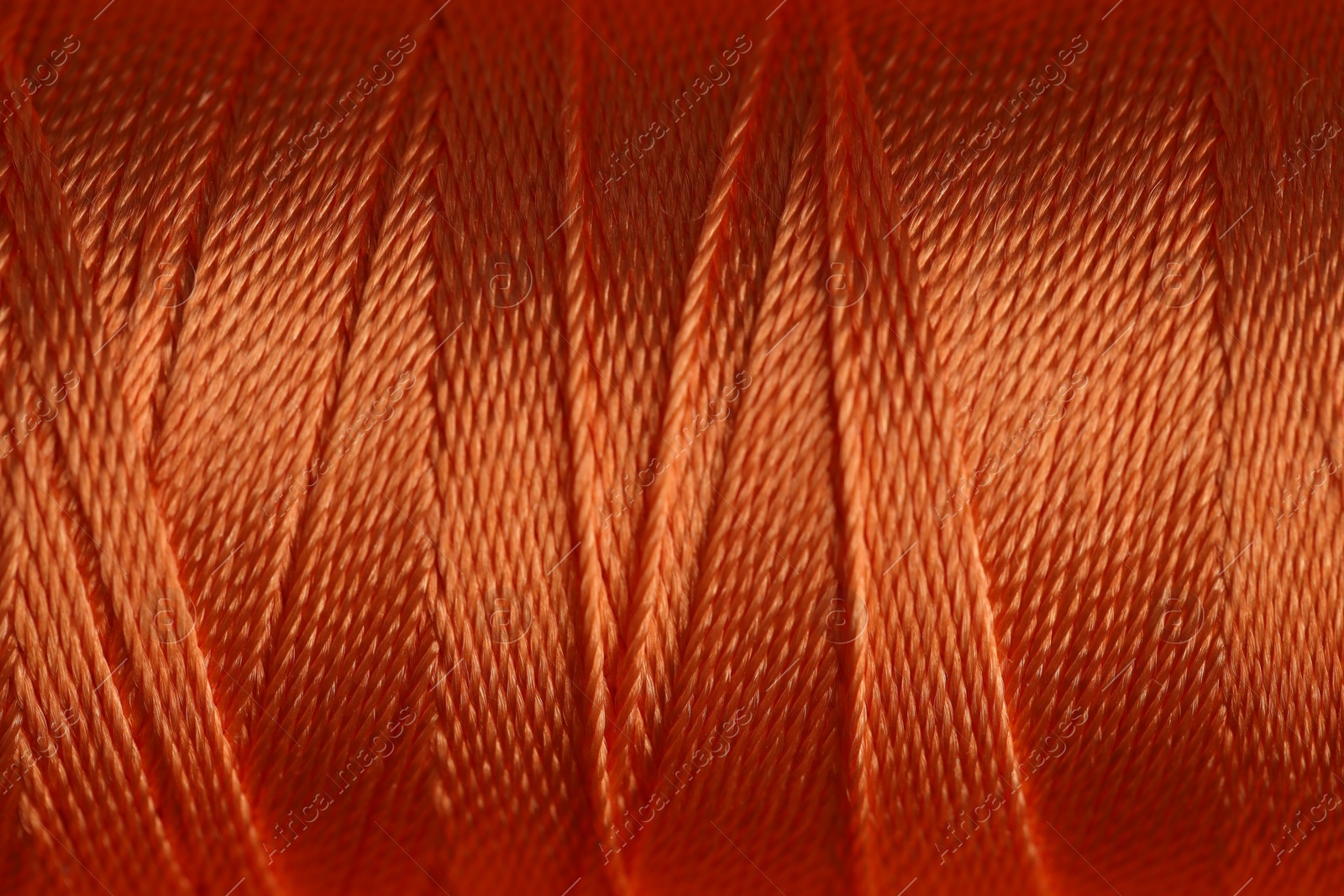 Photo of Spool of orange sewing thread as background, closeup