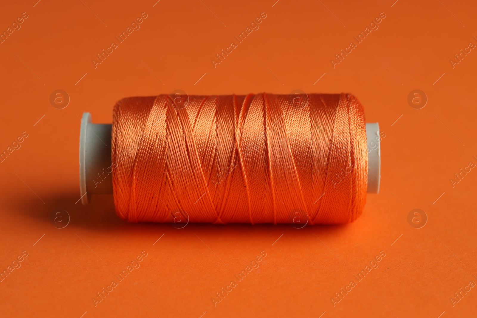 Photo of Spool of sewing thread on orange background, closeup