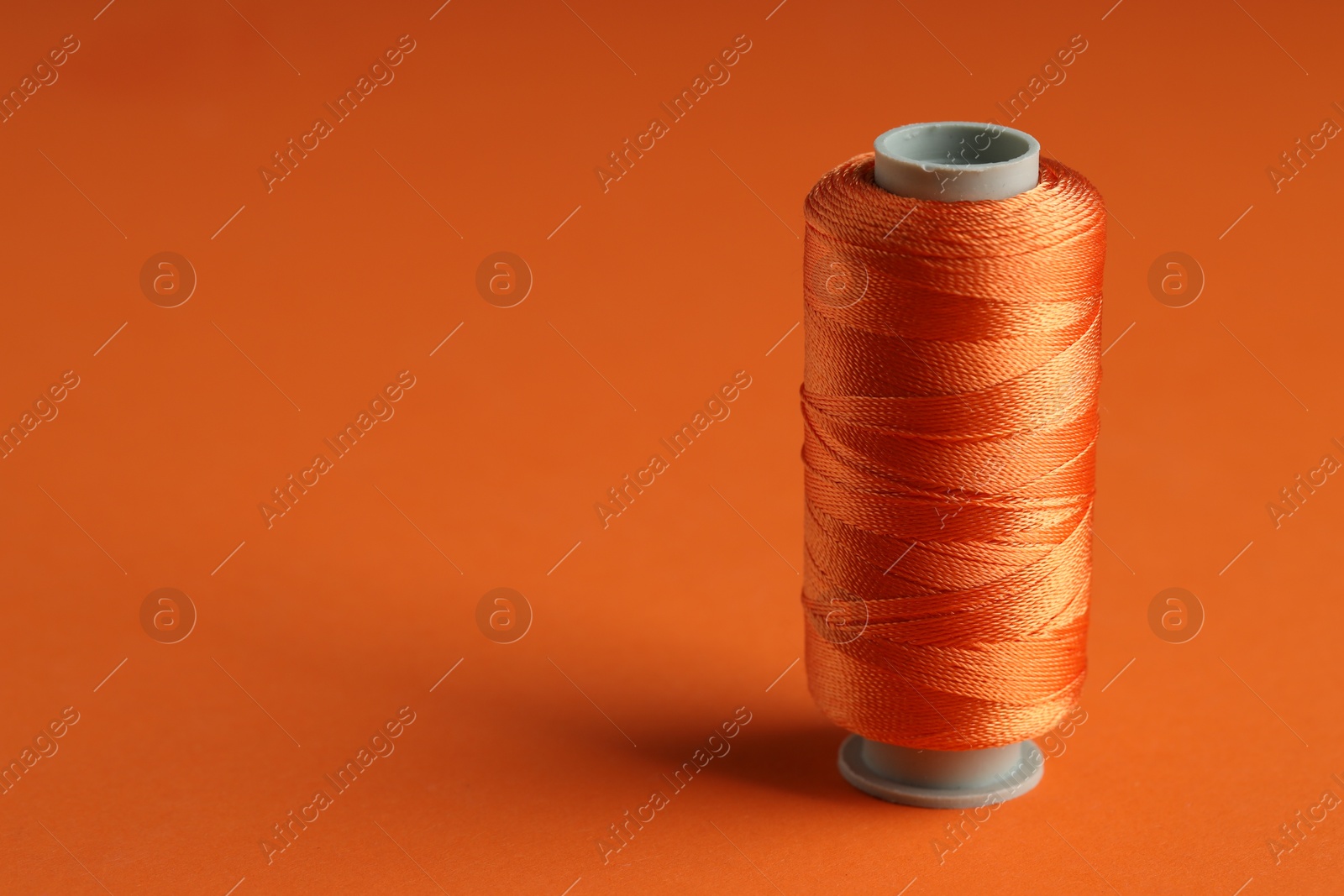 Photo of Spool of sewing thread on orange background, space for text