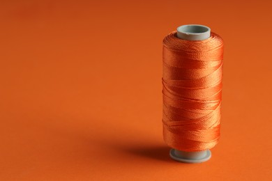 Photo of Spool of sewing thread on orange background, space for text