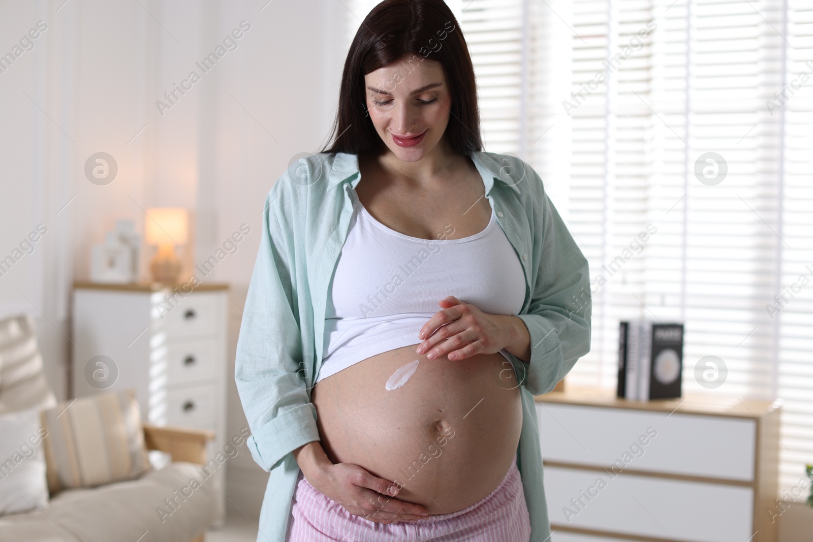 Photo of Beautiful pregnant woman applying cream on belly at home