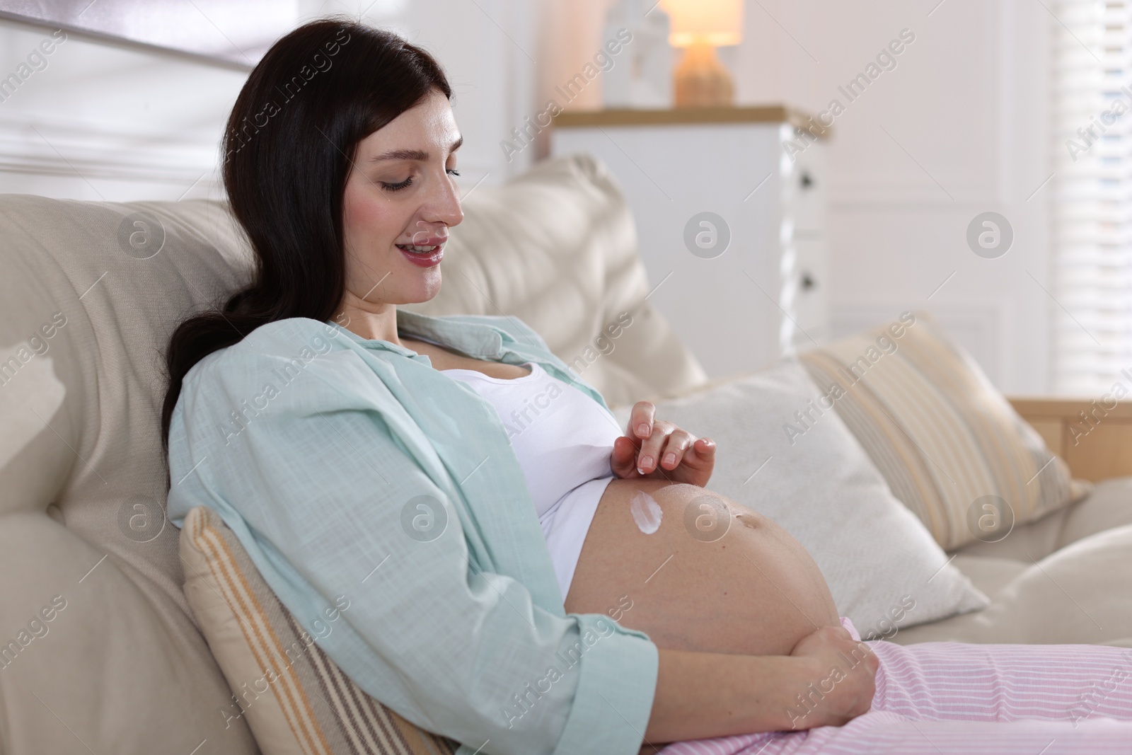 Photo of Beautiful pregnant woman applying cream on belly at home