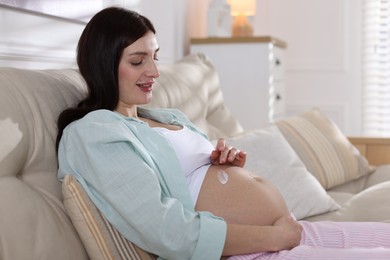 Photo of Beautiful pregnant woman applying cream on belly at home