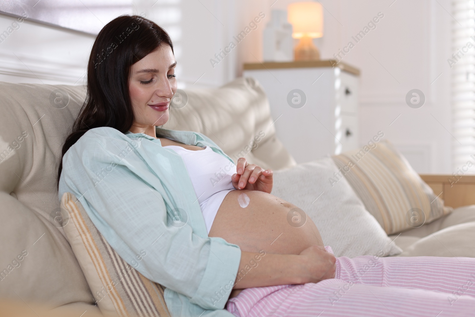 Photo of Beautiful pregnant woman applying cream on belly at home