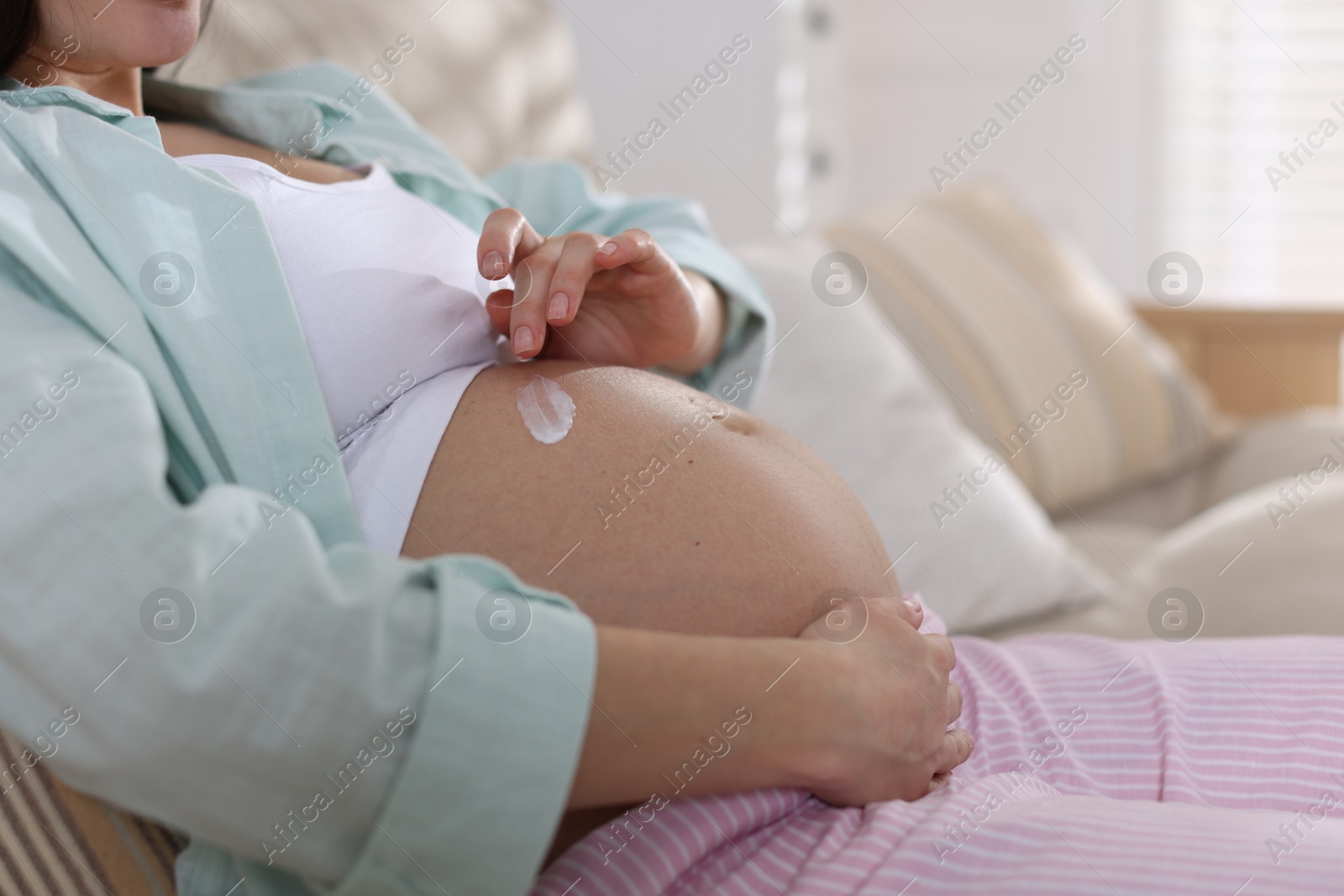 Photo of Pregnant woman applying cream on belly at home, closeup