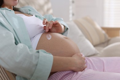 Photo of Pregnant woman applying cream on belly at home, closeup