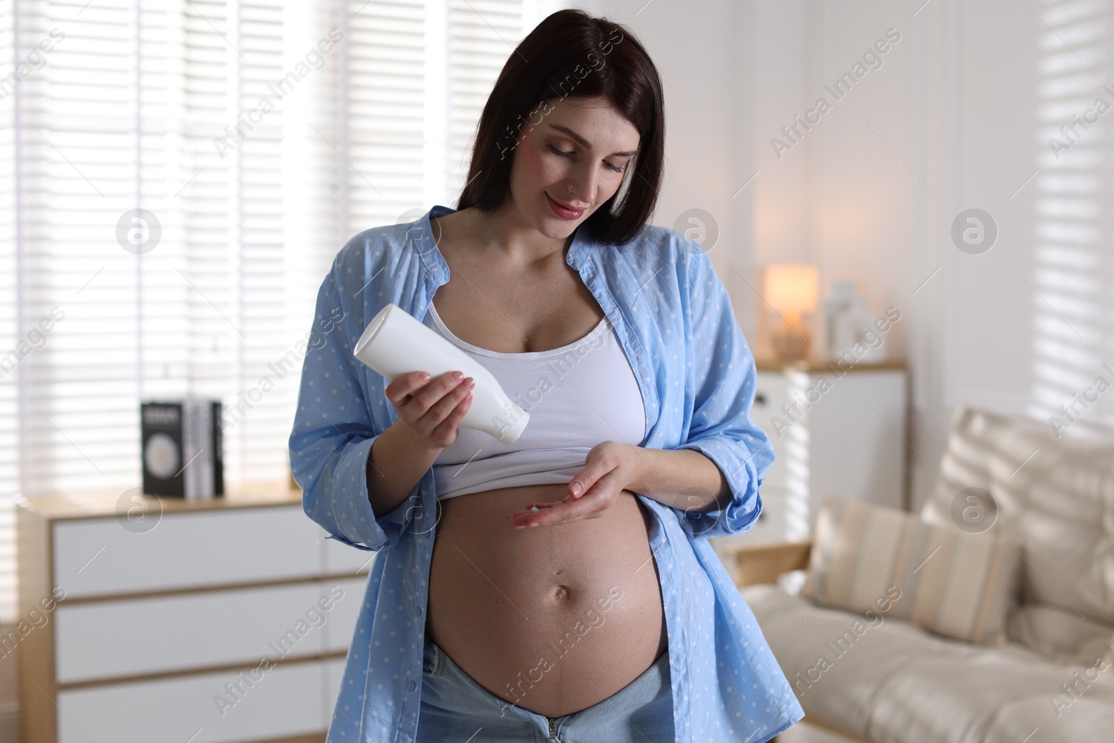 Photo of Beautiful pregnant woman applying cream on belly at home