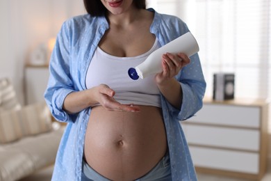 Photo of Pregnant woman applying cream on belly at home, closeup