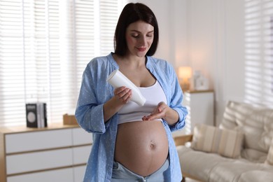 Photo of Beautiful pregnant woman applying cream on belly at home