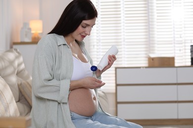 Photo of Beautiful pregnant woman applying cream on belly at home