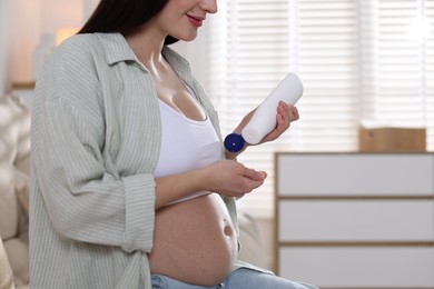 Photo of Pregnant woman applying cream on belly at home, closeup