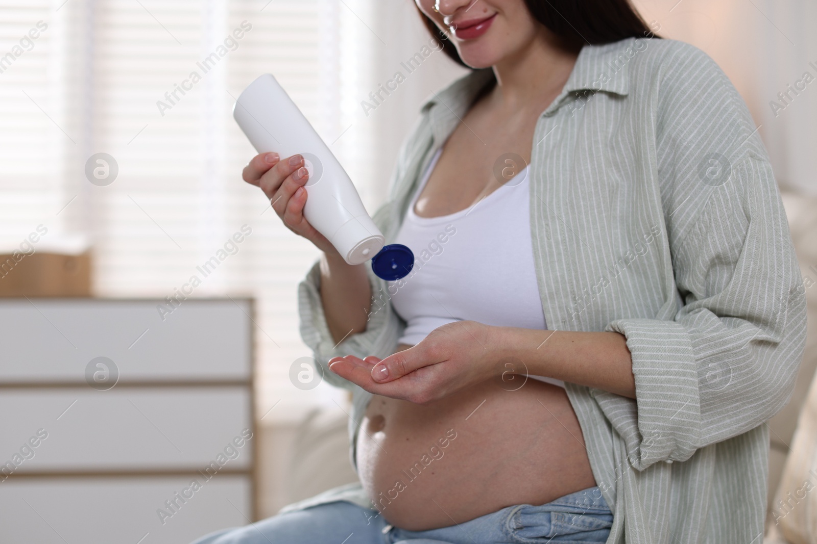 Photo of Pregnant woman applying cream on belly at home, closeup