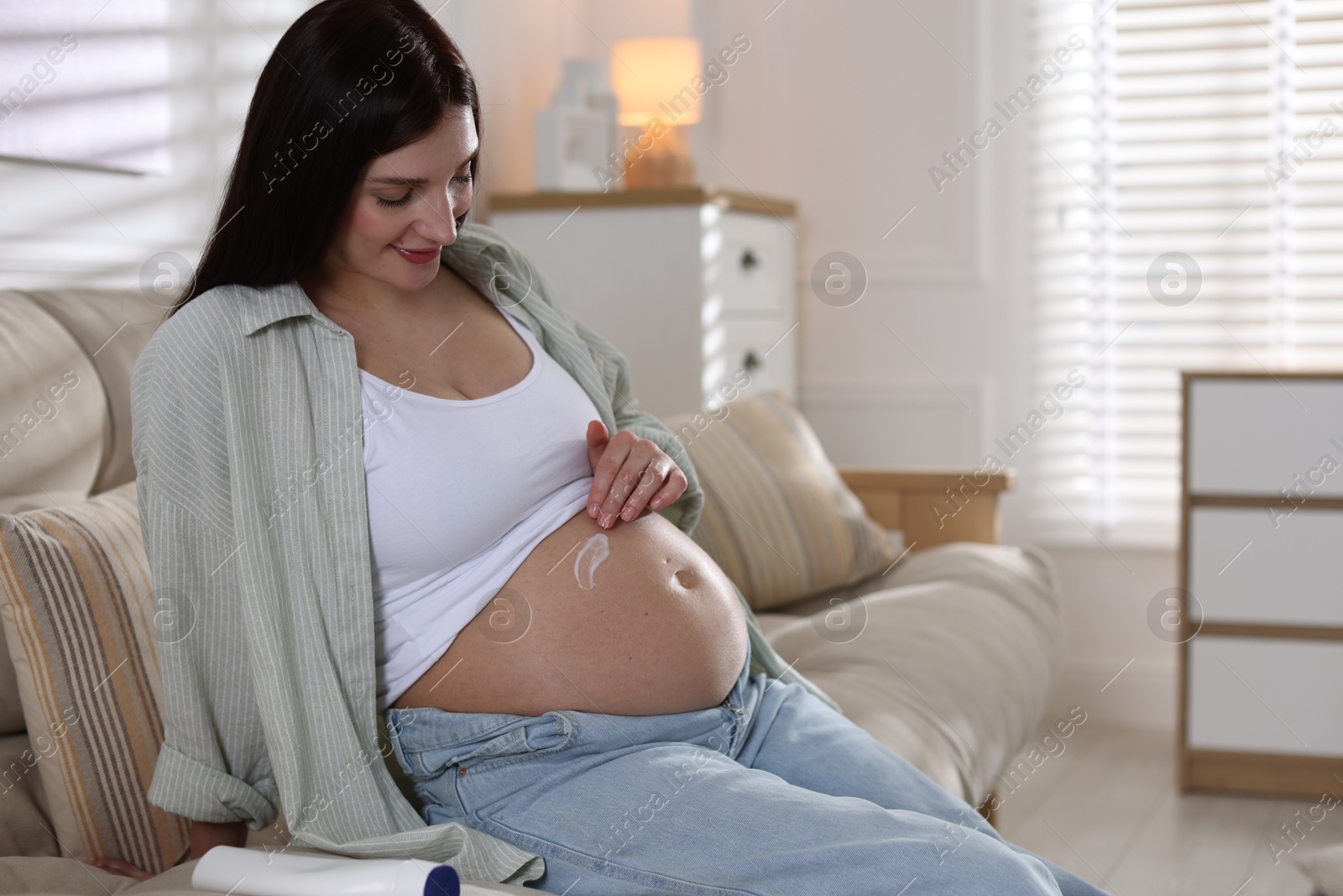 Photo of Beautiful pregnant woman applying cream on belly at home