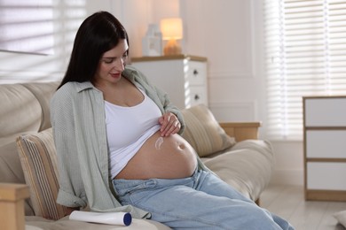 Photo of Beautiful pregnant woman applying cream on belly at home