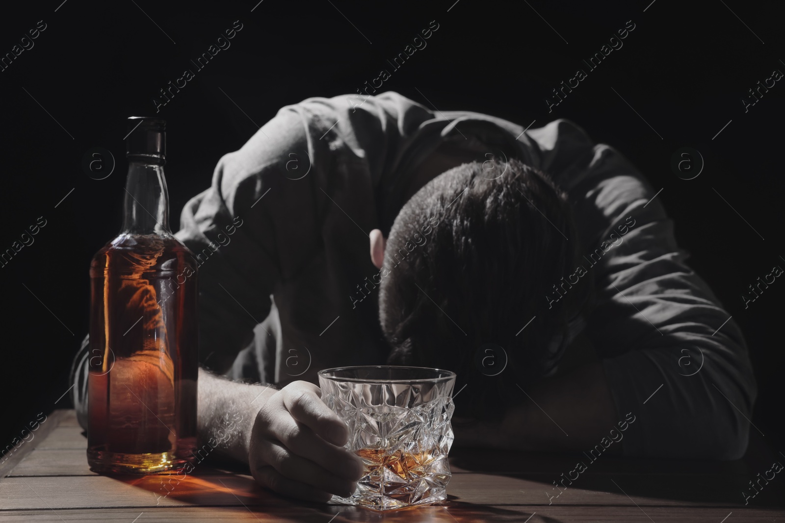 Image of Alcohol addiction. Drunk man with alcohol at table in darkness