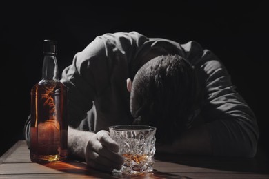 Image of Alcohol addiction. Drunk man with alcohol at table in darkness