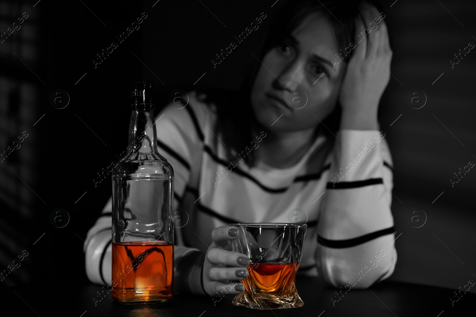 Image of Alcohol addiction. Woman with glass of whiskey and bottle at table